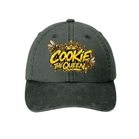 A dark gray washed baseball cap featuring a yellow and gold 'COOKIE THE QUEEN' graphic with bee and crown details on the front